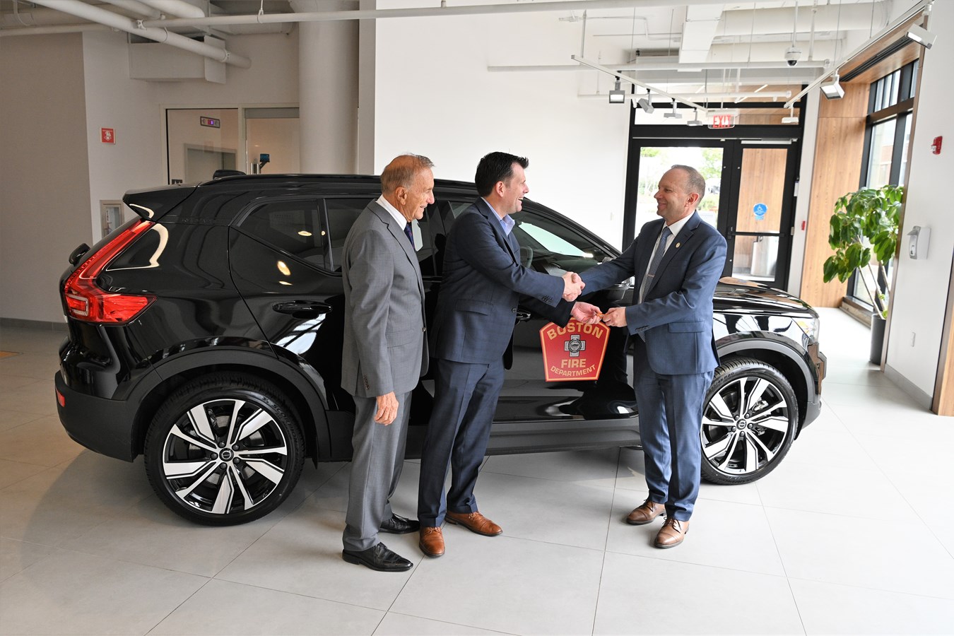 Eric Miller, Vice President Northeast Region, Volvo Car USA, center, hands keys to the Volvo XC40 Recharge electric SUV the company provided BFD for rescue training to Jack Dempsey, Boston Fire Department Fire Commissioner, while Ray Ciccolo, Founder, Village Automotive Group looks on at Boston Volvo Cars in Allston.